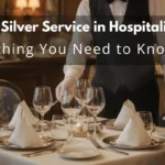 Professional waiter performing silver service, serving guest with fork and spoon in fine dining restaurant.